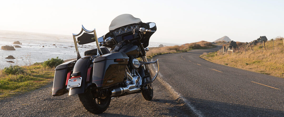 Black Harley-Davidson Street Glide parked on a scenic coastal curve of California Highway 1 near Jenner at sunset.